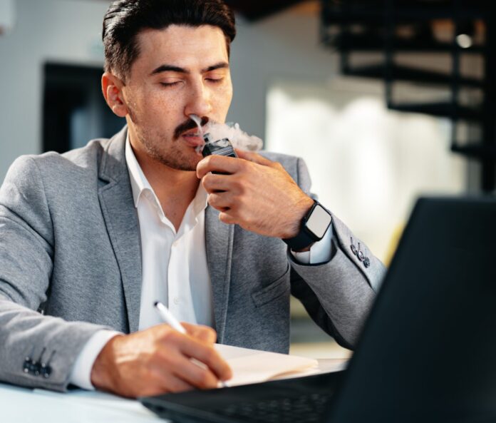 calm man vaping cbd for anxiety in front of laptop