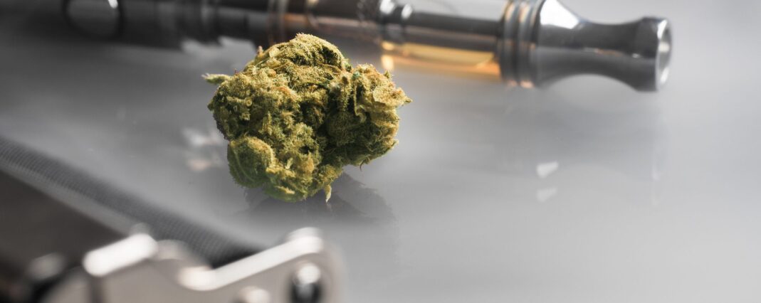 Close up shot of CBD tea flower in the middle, vape pen with CBD oil in the cartridge in the background