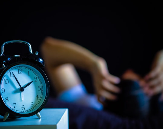 man holding his head behind an alarm clock