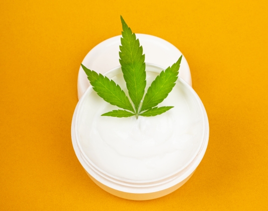 Hemp leaf placed on an open pot of moisturiser