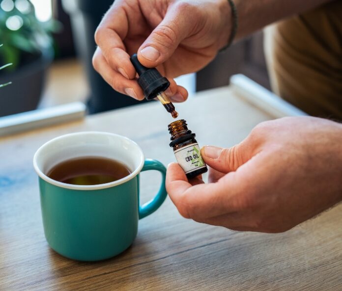 CBD oil bottle being opened over a mug of tea